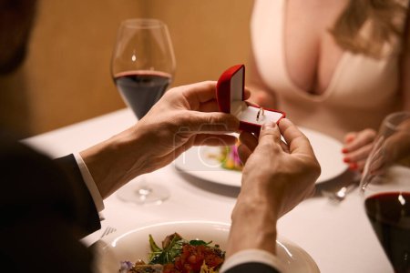 Téléchargez les photos : Homme donne à dame une bague de fiançailles dans une petite boîte rouge, un couple ayant un dîner romantique dans un restaurant - en image libre de droit