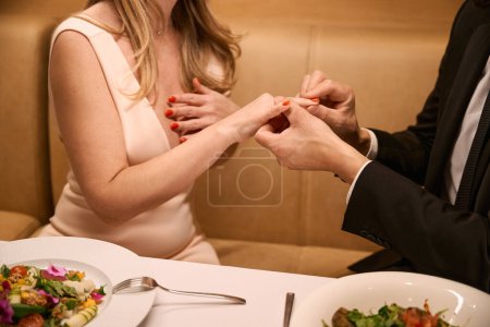 Foto de Hombre pone un anillo de bodas en un dedo de mujer, pareja en un restaurante teniendo una cena romántica - Imagen libre de derechos