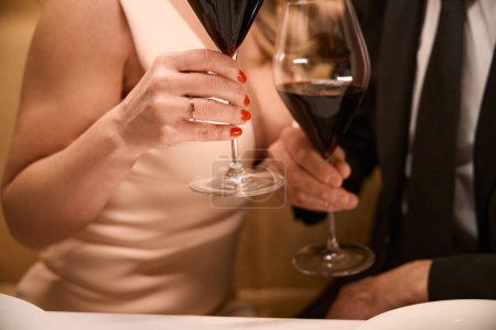 Téléchargez les photos : Couple en robes de soirée avec des verres de vin rouge, la femme a une manucure soignée - en image libre de droit