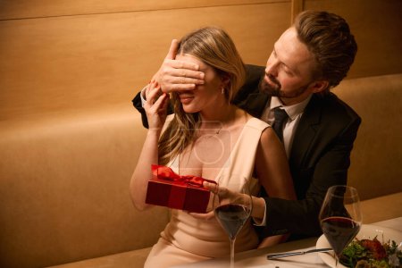 Foto de El hombre organizó una sorpresa para su encantadora compañera en una cena romántica, un regalo en una caja roja - Imagen libre de derechos