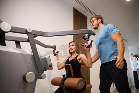 Photo for Patient at a health center is working out on a weight machine under the guidance of an instructor - Royalty Free Image