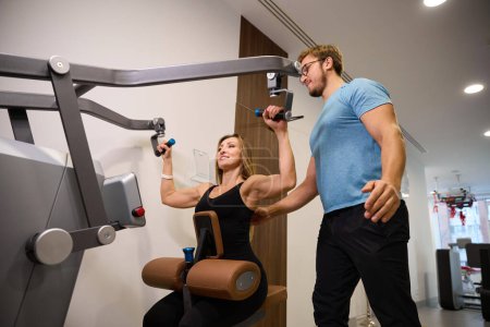 Photo for Woman in a health center works out on a weight machine under the supervision of an instructor - Royalty Free Image