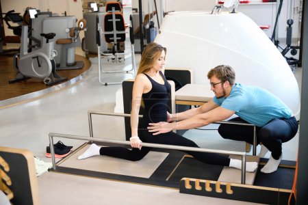 Physiotherapist helps a woman do the splits using a special device