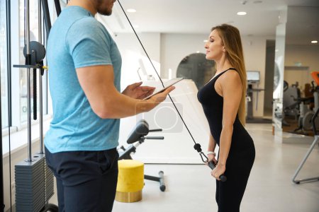 Photo for Lady works on a weight machine under the supervision of an instructor, people in training clothes - Royalty Free Image
