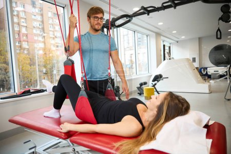 Instructor prepares a woman for a lesson on the redcord, she lies on a red massage table