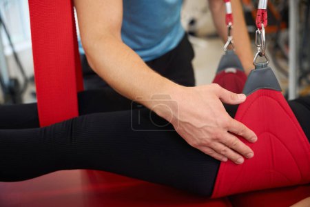 Specialist uses a redcord in a rehabilitation program for a client, she lies on a red massage table