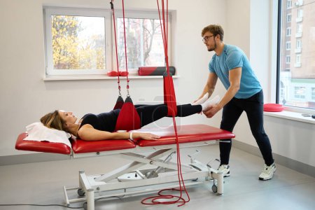 Physiotherapist uses an effective redcord in his work, the patient is secured in a suspension loop system