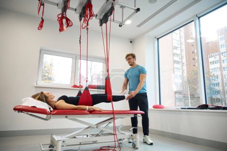 Rehabilitation specialist uses an effective redcord in his work, the patient is secured in a hanging loop system