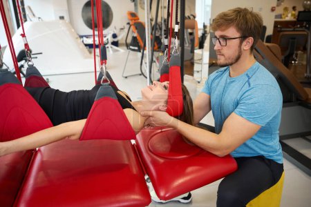 Spezialist für Kinesiologie fixiert eine Frau in einem Schwebeschlaufensystem mit modernen Heilungstechniken an einem Rotstrang
