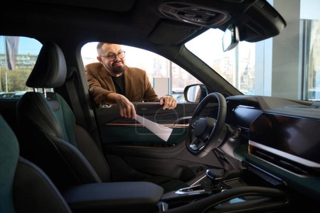 Téléchargez les photos : L'homme regarde à l'intérieur d'une voiture neuve chez un concessionnaire - en image libre de droit