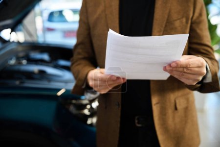 Téléchargez les photos : Homme adulte tient entre ses mains un contrat pour l'achat d'une voiture neuve dans un concessionnaire automobile - en image libre de droit