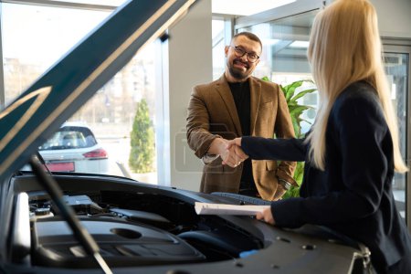 Téléchargez les photos : Guy acheteur serre la main avec le vendeur de voiture près de voiture neuve - en image libre de droit