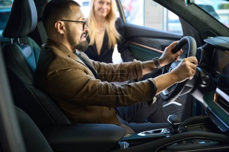 Foto de El tipo con gafas toca el volante del coche que quiere comprar - Imagen libre de derechos