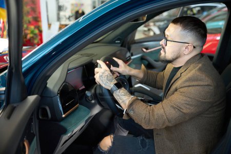 Téléchargez les photos : Homme assis sur le siège avant d'une voiture dans une salle d'exposition de voiture - en image libre de droit