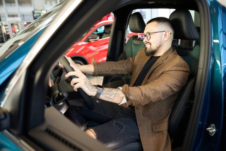 Téléchargez les photos : Un homme vêtu d'une veste est assis dans une nouvelle voiture au volant - en image libre de droit