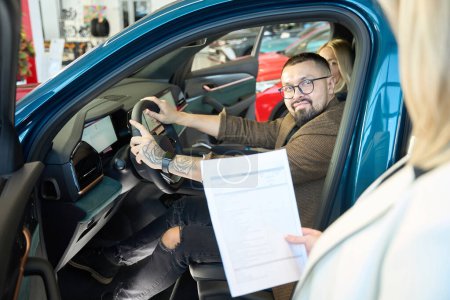 Téléchargez les photos : Femme blonde qui vend des voitures détient un contrat pour l'achat d'une nouvelle voiture dans ses mains - en image libre de droit