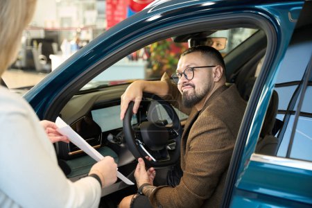 Foto de Hombre sentado detrás del volante de un coche se comunica con el vendedor - Imagen libre de derechos