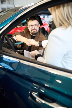 Téléchargez les photos : Un jeune homme assis dans une voiture serre la main d'un conseiller commercial - en image libre de droit