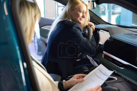 Foto de Mujer vendedor de coches tiene un contrato para la compra de un coche mientras mira a la mujer comprador - Imagen libre de derechos