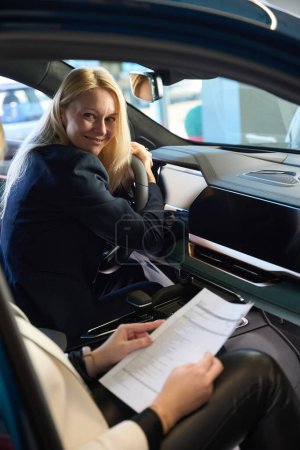 Foto de Jovencita se sienta en un coche nuevo abrazando el volante del coche - Imagen libre de derechos