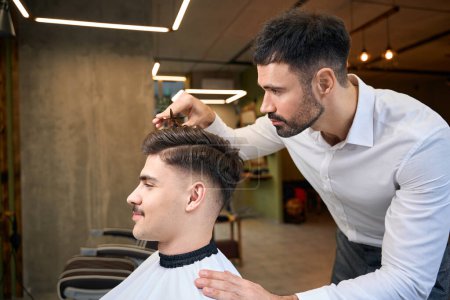 Téléchargez les photos : Homme client ayant ses cheveux coupés par le coiffeur au salon de beauté - en image libre de droit