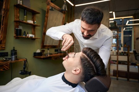 Téléchargez les photos : Coiffeur professionnel faisant moustache coiffure pour homme client dans le salon de coiffure - en image libre de droit