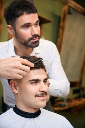 Téléchargez les photos : Homme coiffeur servant client avec moustache au salon de coiffure - en image libre de droit