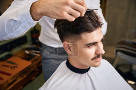 Téléchargez les photos : Coiffeur méconnaissable subissant une coiffure pour jeune client au salon de beauté - en image libre de droit