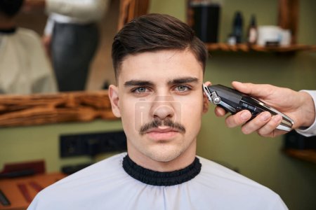 Téléchargez les photos : Coiffeur utilisant une tondeuse à cheveux pour faire une coiffure élégante au salon de coiffure - en image libre de droit