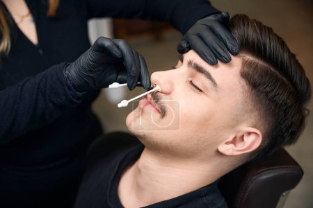Téléchargez les photos : Maître barbier méconnaissable enlève les cheveux du nez de l'homme avec de la cire dans le salon de coiffure - en image libre de droit