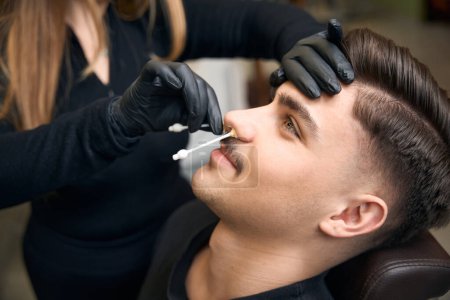 Foto de Maestro peluquero quitar el pelo de la nariz del hombre haciendo depilación procedimiento de belleza en la barbería - Imagen libre de derechos