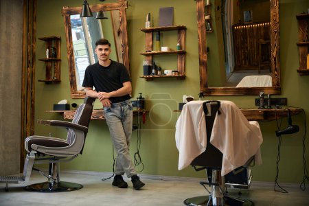 Téléchargez les photos : Barbier professionnel debout sur son lieu de travail dans le salon de coiffure - en image libre de droit