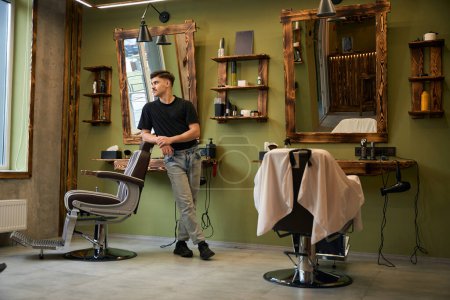 Téléchargez les photos : Coiffeur professionnel debout sur son lieu de travail dans le salon de coiffure - en image libre de droit