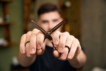 Photo for Blurred barber showing scissors while standing in barbershop - Royalty Free Image