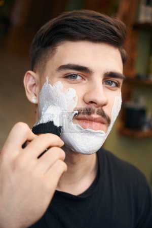 Foto de Sonriente hombre guapo peluquero afeitarse en la barbería - Imagen libre de derechos