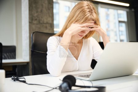 Téléchargez les photos : Femme fatiguée dans casque de communication avec le client dans les ventes en ligne au bureau - en image libre de droit