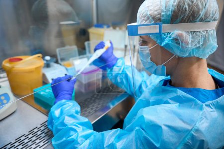 Female infectious disease specialist working in laboratory with biomaterial, woman uses protective gadgets