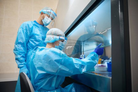 Foto de Personal de laboratorio analiza biomaterial en una habitación estéril, utilizando dispositivos de protección - Imagen libre de derechos