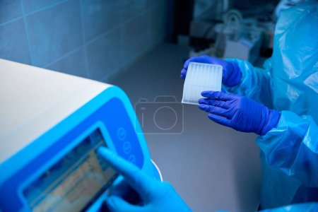 Foto de Asistentes de laboratorio trabajan en una máquina para el aislamiento automático de ácidos nucleicos, las personas que usan guantes de protección - Imagen libre de derechos