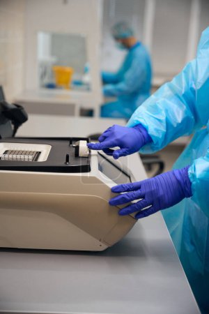 Asistente de laboratorio lleva a cabo la investigación en un laboratorio moderno, la gente trabaja en guantes de protección