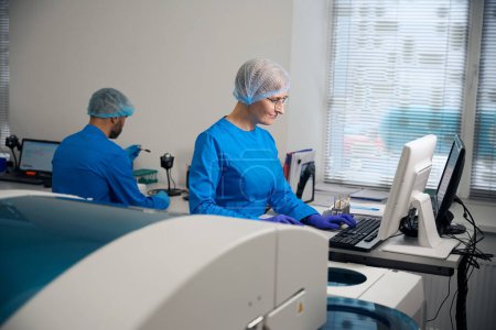 Asistentes de laboratorio de hombre y mujer usan computadoras modernas en el trabajo, personas con uniformes azules