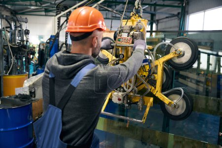 Photo for Man wearing protective gloves works in a window production workshop, he uses a vacuum lifting device - Royalty Free Image