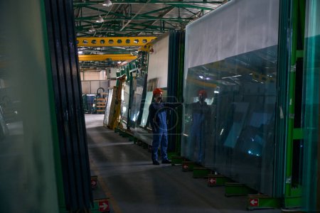 Foreman inspects glass in a window production workshop, a man in an orange safety helmet