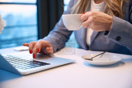 Foto de Empresaria de mediana edad se sienta en la ventana de la vista con un ordenador portátil, ella bebe café - Imagen libre de derechos