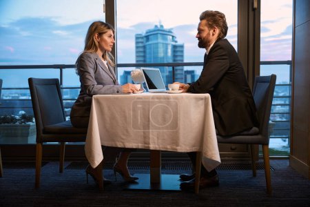 Foto de Elegante pareja discutiendo un proyecto de negocio sobre café, portátil sobre la mesa - Imagen libre de derechos