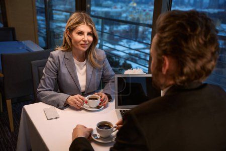 Téléchargez les photos : Femme d'affaires souriante parlant autour d'un café avec un partenaire d'affaires, ordinateur portable sur la table - en image libre de droit