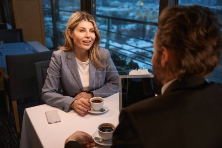 Téléchargez les photos : Femme d'affaires d'âge moyen parle autour d'un café avec un partenaire d'affaires, il y a un ordinateur portable sur la table - en image libre de droit