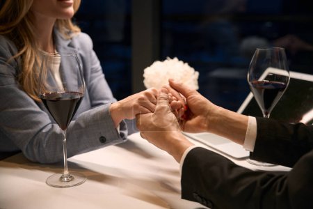 Foto de El hombre sostiene suavemente las manos de una dama, una pareja en un restaurante tomando una copa de vino - Imagen libre de derechos