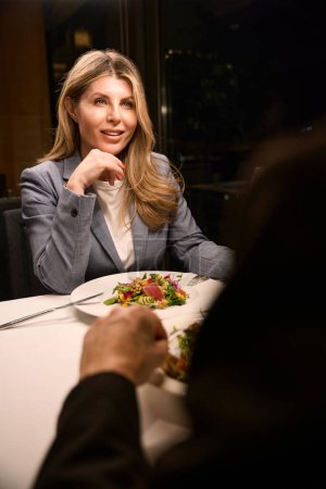 Téléchargez les photos : Femme d'affaires dînant dans un restaurant confortable avec un partenaire d'affaires, salade légère sur des assiettes - en image libre de droit