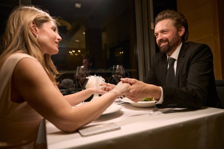 Foto de Una pareja se sienta en una mesa en un restaurante, la gente se toma de la mano - Imagen libre de derechos